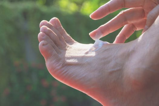 hand of woman apply lotion on skin of back foot on nature background.