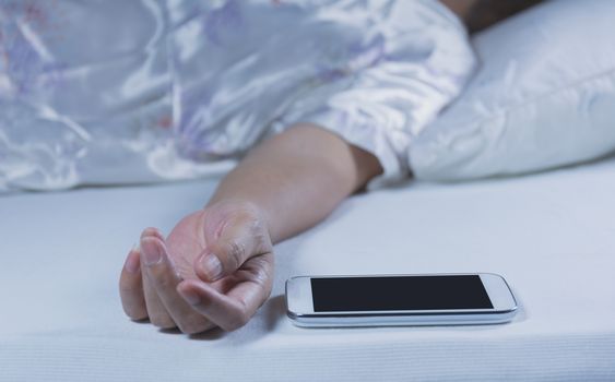 Woman sleeping with a mobile phone on the bed in bedroom, she is resting with eyes closed.