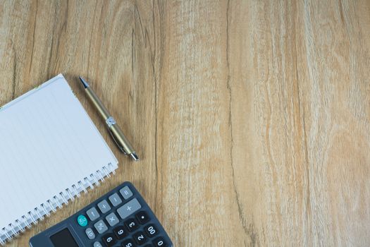 Top view of note book, pen and calculator on wooden table background with copy space.