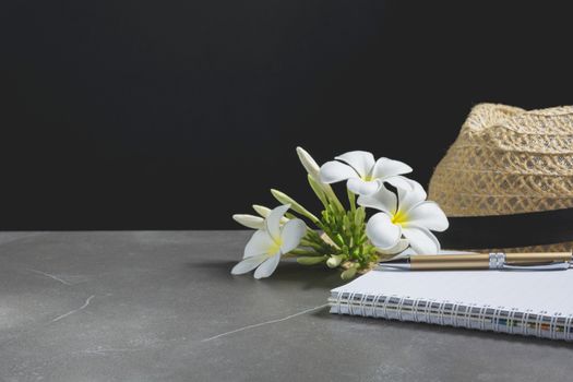Open notebook with hat. Book open, with pen and flower on table dark tone background.