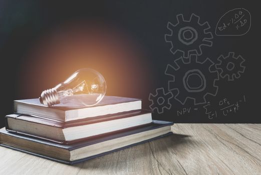 Pile of book with glowing light bulb over it on wood wall background. Knowledge, education concept.