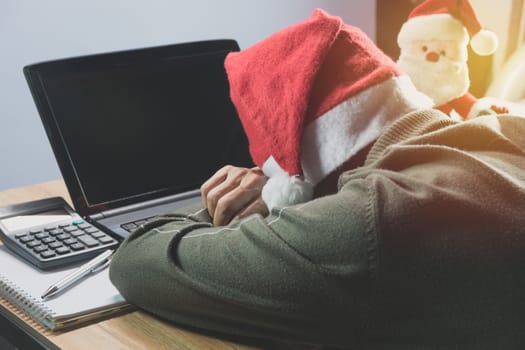 Female wearing Santa Claus red hat sleeping with laptop and Santa Claus doll in Christmas day.