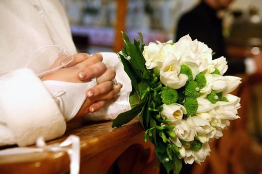 Hands of the bride and groom in the background praying in church at wedding ceremony.