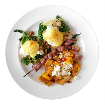 Poached eggs in hollandaise sauce, also called Eggs Benedict, with one beef skewer, mushrooms, squash, and crumbled cheese, isolated on white background.