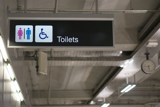 Toilets information board sign with white character on black background have blur clock and loudspeaker at international airport terminal.