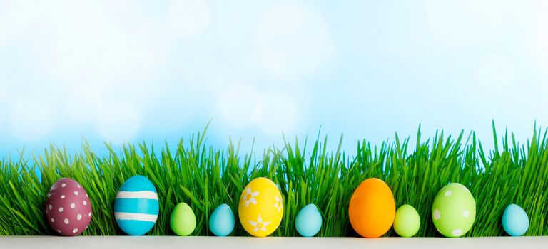 Row of Easter Eggs in fresh green grass over blue sky background