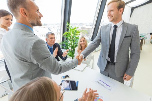 Handshake at business meeting in office, people on background applauding