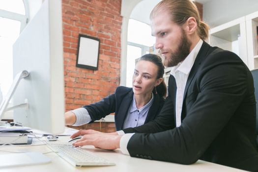 Two business people using computer together in office pointing at monitor