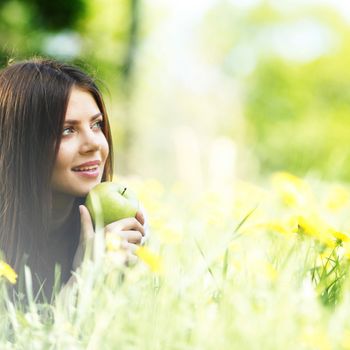 Young beautiful woman with apple resting on fresh green grass with flowers