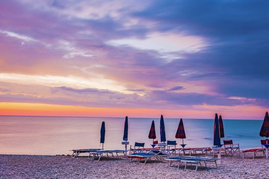 sunrise in a stony beach with umbrellas and sunbeds