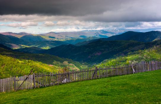 fence on the edge of the hillside. beautiful rural landscape of Carpathian mountains in springtime. forested hills under the heavy clouds in the distance