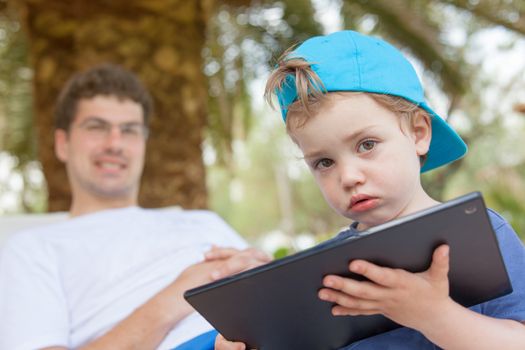 Little boy with dirty mouth is playing with his father tablet outdoors.