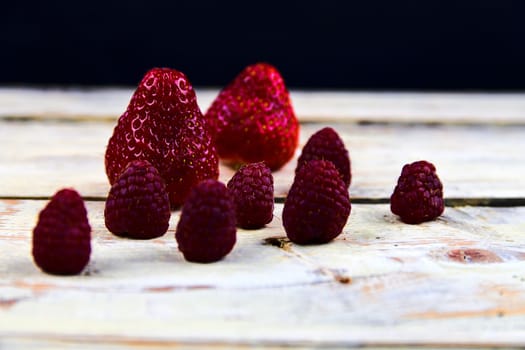 Strawberries and raspberries on rustic white wooden background. White and black background. Dark image. 