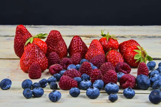 Healthy mixed fruit and ingredients with strawberry, raspberry, blueberry. Berries on rustic white wooden background. Free space for text. Copy space for banner.