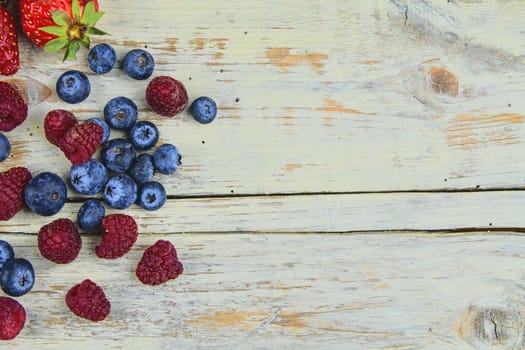 Healthy mixed fruit and ingredients with strawberry, raspberry, blueberry from top view. Berries on rustic white wooden background. Flat design. Free space for text. Copy space for banner.