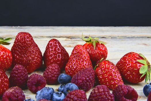 Healthy mixed fruit and ingredients with strawberry, raspberry, blueberry. Berries on rustic white wooden background. Free space for text. Copy space for banner.
