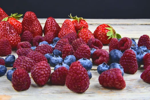 Healthy mixed fruit and ingredients with strawberry, raspberry, blueberry. Berries on rustic white wooden background. Free space for text. Copy space for banner.