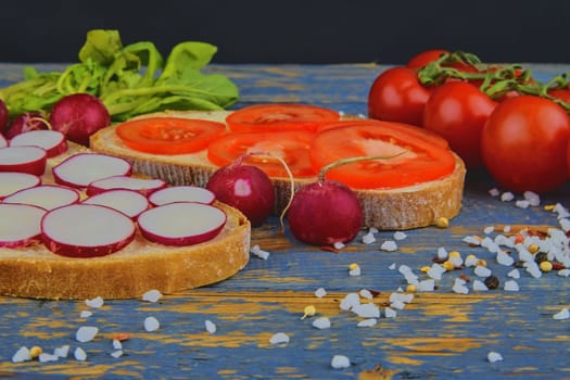 Spread butter on bread with sliced tomatoes and radishes. Fresh snack on natural wooden background. 