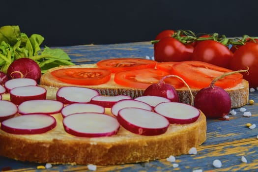 Spread butter on bread with sliced tomatoes and radishes. Fresh snack on natural wooden background.