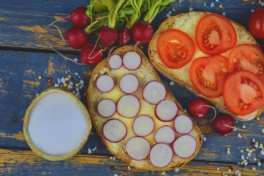 Spread butter on bread with sliced tomatoes and radishes. Fresh snack on natural wooden background. Flat design. Top view.