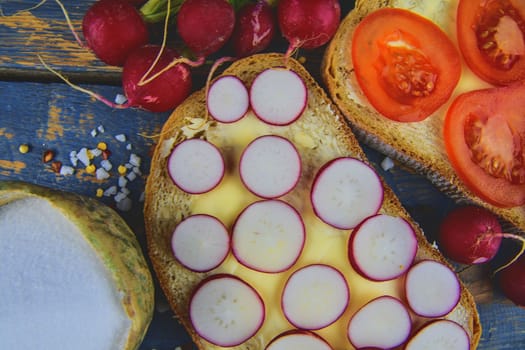 Spread butter on bread with sliced tomatoes and radishes. Fresh snack on natural wooden background. Flat design. Top view.