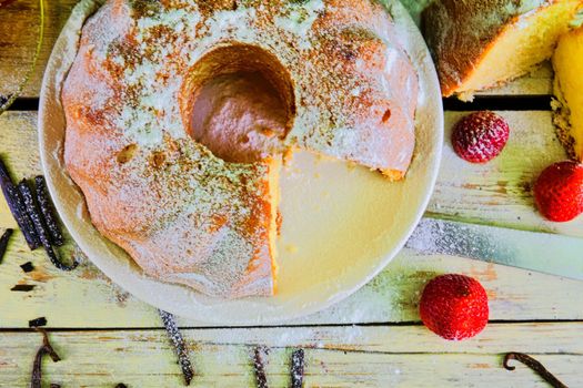 Old fashioned sand cake with cup of black tea and pieces of vanilla on wooden background. Egg-yolk sponge cake with stawberries on rustic white background. Top view. Flat design.