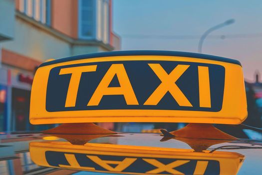 Lit taxi sign on roof of taxi car in the city.