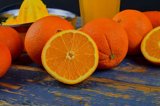 Tangerines, oranges, a glass of orange juice and manual citrus squezeer on blue wooden background. Oranges cut in half.