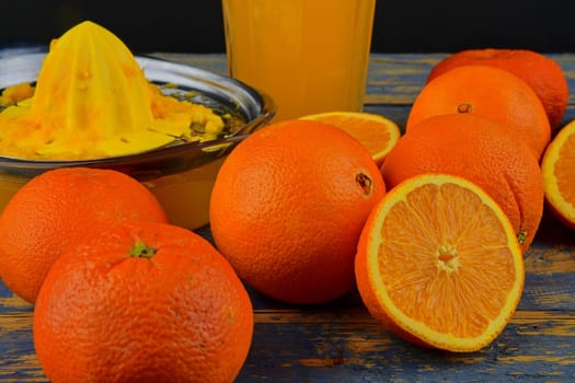 Tangerines, oranges, a glass of orange juice and manual citrus squezeer on blue wooden background. Oranges cut in half.