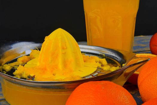 Tangerines, oranges, a glass of orange juice and manual citrus squezeer on blue wooden background. Oranges cut in half.