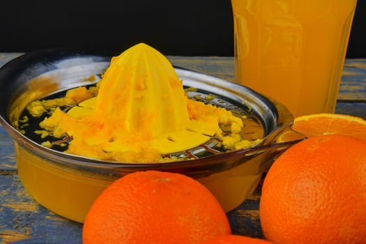 Tangerines, oranges, a glass of orange juice and manual citrus squezeer on blue wooden background. Oranges cut in half.