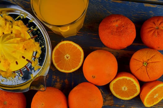 Tangerines, oranges, a glass of orange juice and manual citrus squezeer on blue wooden background. Oranges cut in half. Top view, flat design.