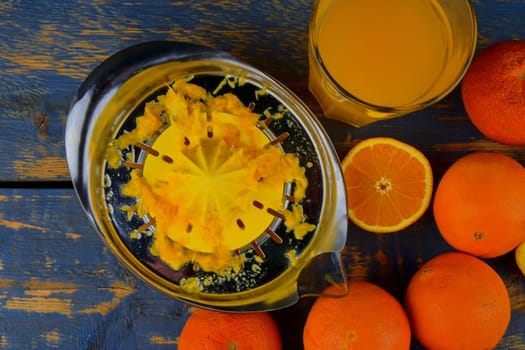 Tangerines, oranges, a glass of orange juice and manual citrus squezeer on blue wooden background. Oranges cut in half. Top view, flat design.