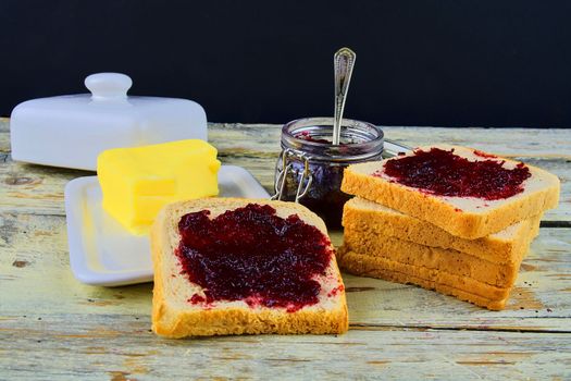 Jam, butter in butter dish and jam spread on toast. Healthy and diet concept. Rural white wooden background.