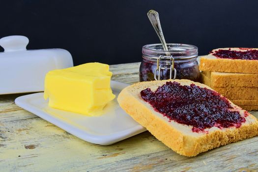 Jam, butter in butter dish and jam spread on toast. Healthy and diet concept. Rural white wooden background.