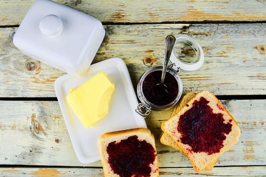 Jam, butter in butter dish and jam spread on toast. Healthy and diet concept. Rural white wooden background. Flat design, top view.