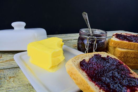 Jam, butter in butter dish and jam spread on toast. Healthy and diet concept. Rural white wooden background.