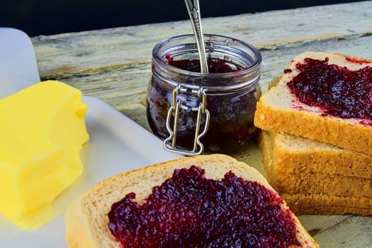 Jam, butter in butter dish and jam spread on toast. Healthy and diet concept. Rural white wooden background.