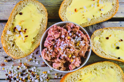 Slices of baguettes with butter and  fresh tuna with spices on wooden background. Top view. Flat design. 