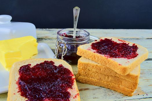 Jam, butter in butter dish and jam spread on toast. Healthy and diet concept. Rural white wooden background.