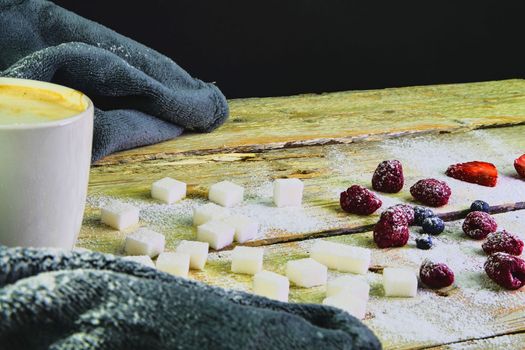 Cup of coffee, sugar cubes, blueberries and strawberries on wooden background. Winter or Valentines day concept.