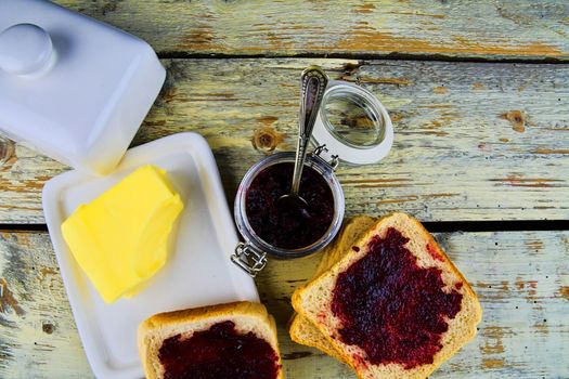 Jam, butter in butter dish and jam spread on toast. Healthy and diet concept. Rural white wooden background. Flat design, top view.