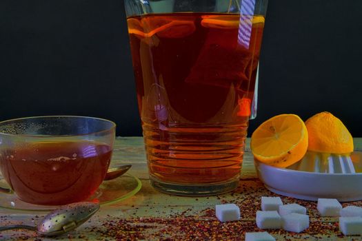 Black tea, a cup of black tea, manual squeezer with lemons. A jug of black tea and cubes of sugar. Dark image. 