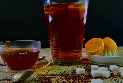 Black tea, a cup of black tea, manual squeezer with lemons. A jug of black tea and cubes of sugar. Dark image. 