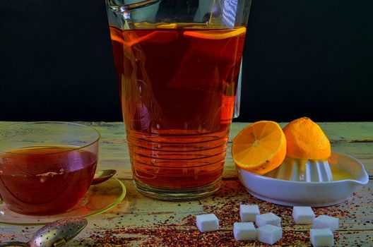 Black tea, a cup of black tea, manual squeezer with lemons. A jug of black tea and cubes of sugar. Dark image. 