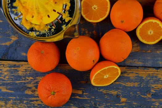 Tangerines, oranges, a glass of orange juice and manual citrus squezeer on blue wooden background. Oranges cut in half. Top view, flat design.