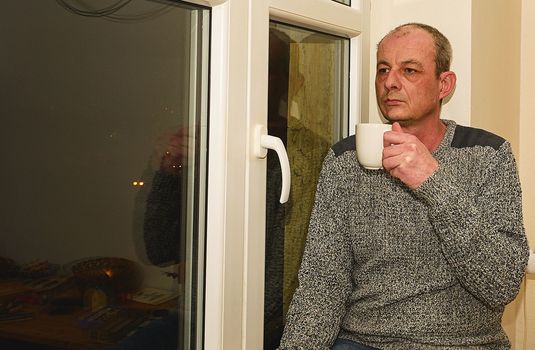 Depressed middle age man sitting near window. Sad man drinking coffee. 