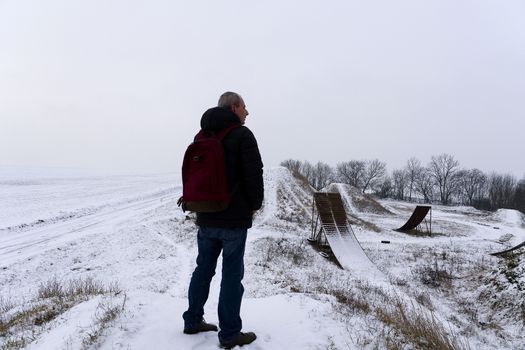 Man viewing on abandoned freestyle motocross ramps. Middle age man standing in winter landscape.