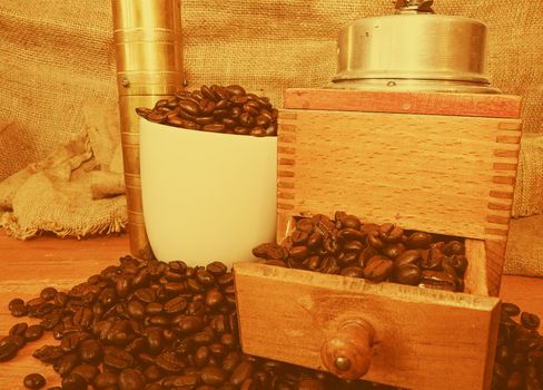 Vintage coffee mills, coffee beans and white cup filled coffee beans on wooden background. 