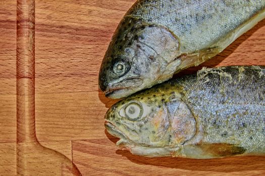 Two raw rainbow trouts on wooden board. Healthy food and dieting concept. Add dark contrasts. Close-up.